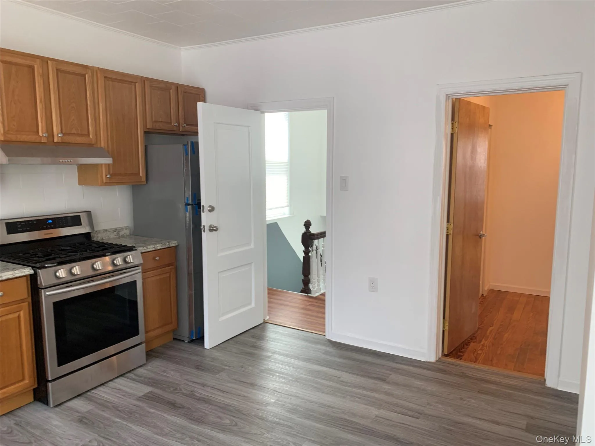 Kitchen featuring stainless steel appliances, brown cabinets, dark wood-type flooring, and ornamental molding Kitchen featuring stainless steel appliances, brown cabinets, dark wood-type flooring, and ornamental molding