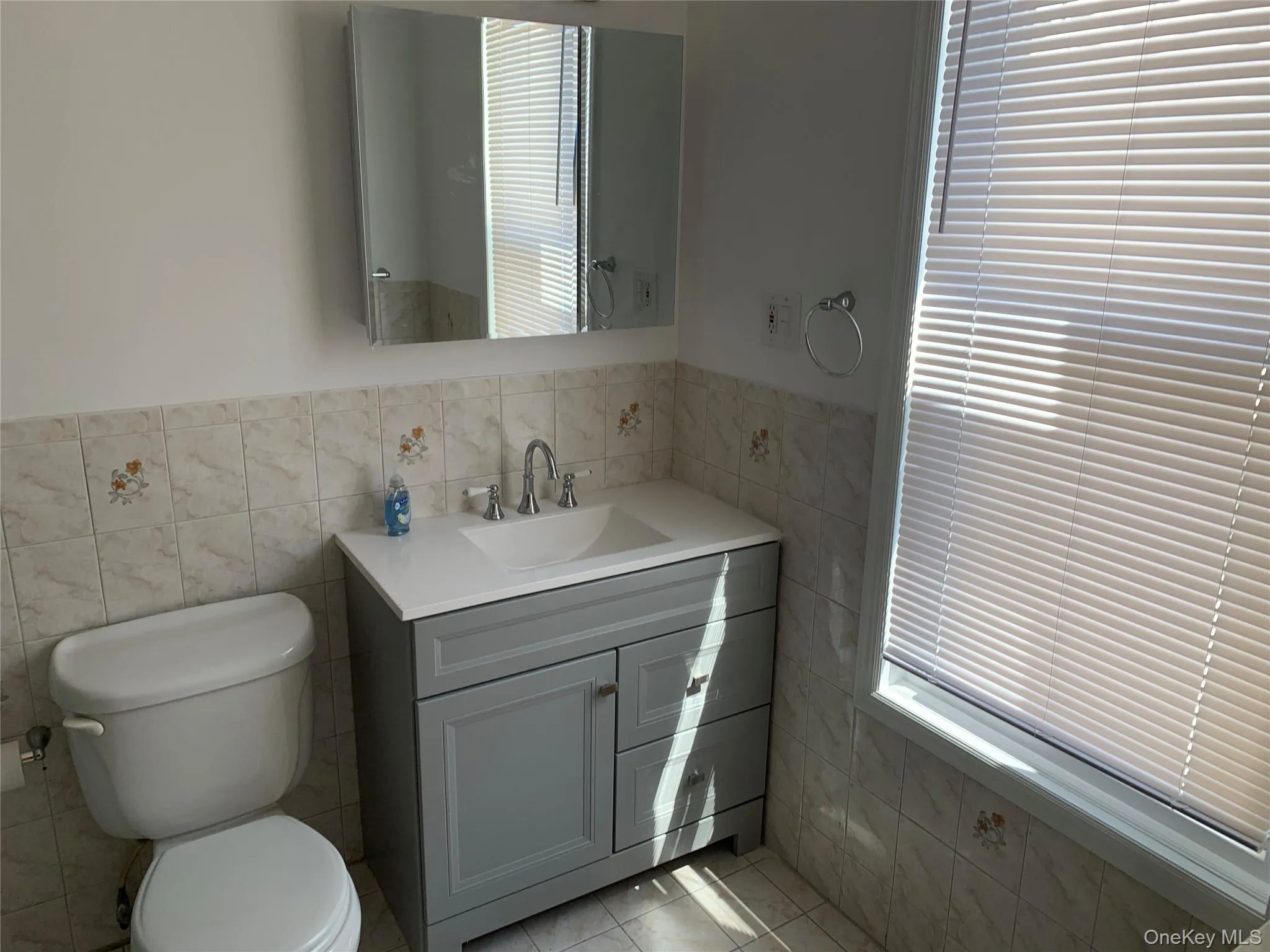 Bathroom featuring vanity, tile walls, healthy amount of natural light, light tile patterned floors, and a wainscoted wall Bathroom featuring vanity, tile walls, healthy amount of natural light, light tile patterned floors, and a wainscoted wall