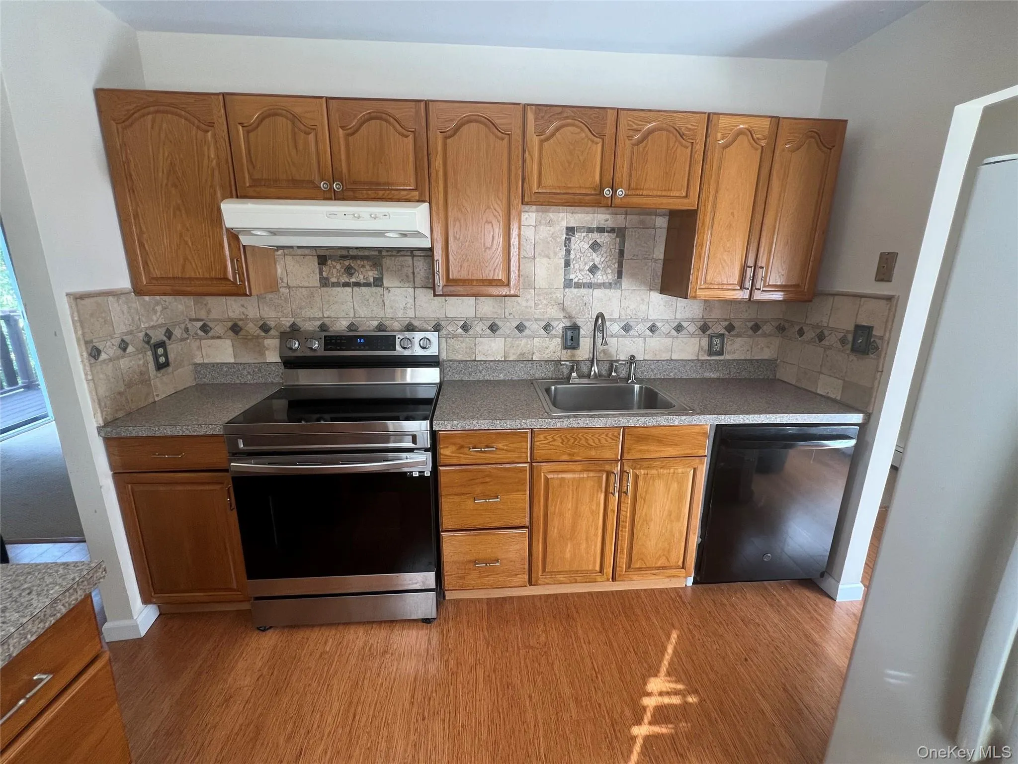 Kitchen with brown cabinets, stainless steel range with electric stovetop, dishwasher, backsplash, and wood finished floors Kitchen with brown cabinets, stainless steel range with electric stovetop, dishwasher, backsplash, and wood finished floors
