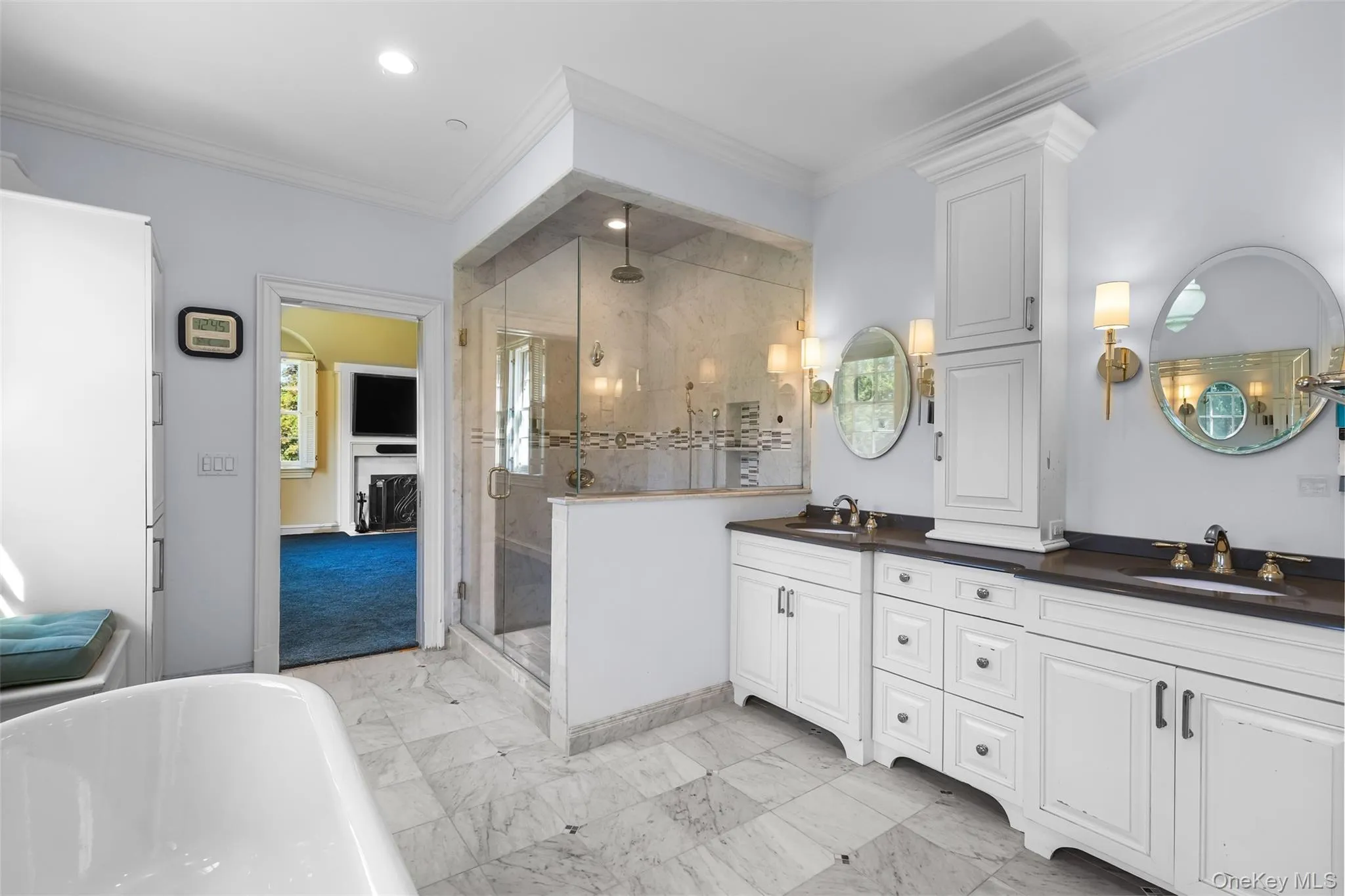 Full bath with a shower stall, ornamental molding, a freestanding tub, double vanity, and light marble finish flooring Full bath with a shower stall, ornamental molding, a freestanding tub, double vanity, and light marble finish flooring