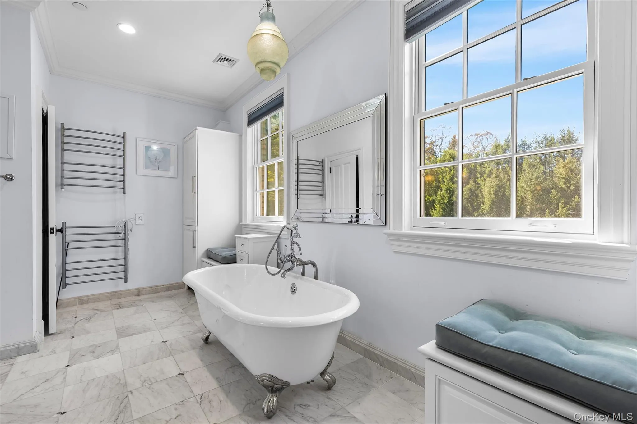 Bathroom featuring a towel warmer, a freestanding bath, ornamental molding, light marble finish floors, and vanity Bathroom featuring a towel warmer, a freestanding bath, ornamental molding, light marble finish floors, and vanity