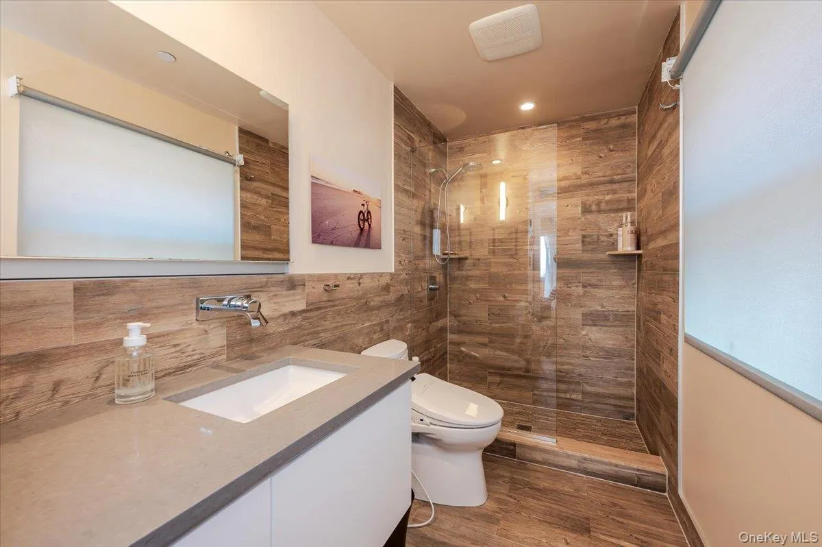 Bathroom featuring vanity, a walk in shower, dark wood-style flooring, and tile walls Bathroom featuring vanity, a walk in shower, dark wood-style flooring, and tile walls