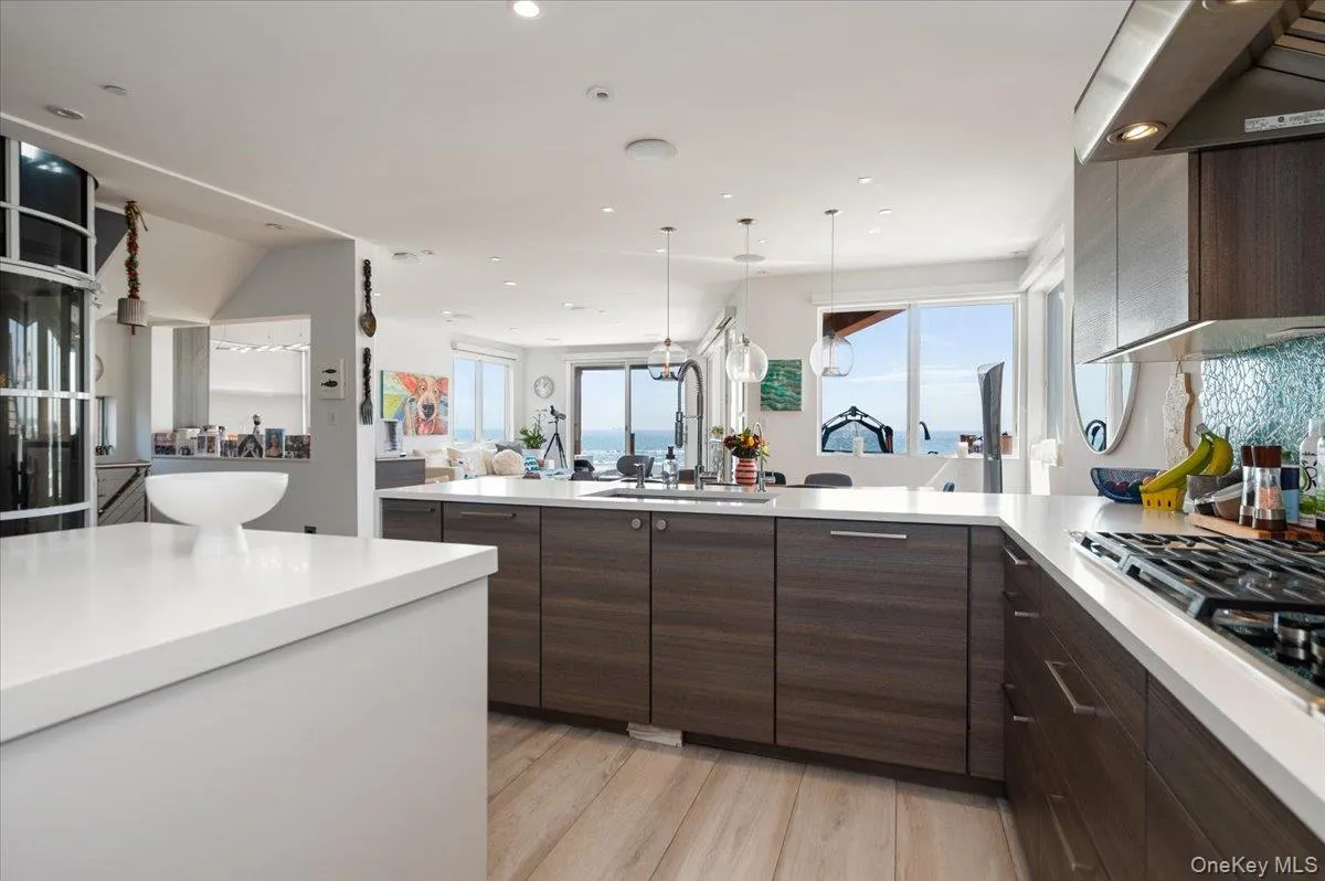 Kitchen with dark brown cabinets, ventilation hood, open floor plan, light wood finished floors, and decorative light fixtures Kitchen with dark brown cabinets, ventilation hood, open floor plan, light wood finished floors, and decorative light fixtures