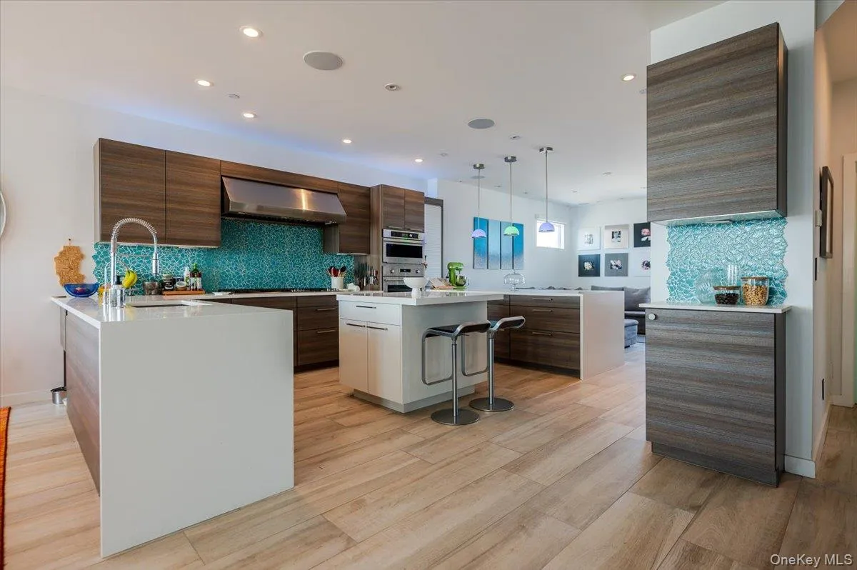 Kitchen with a kitchen breakfast bar, a peninsula, light stone counters, backsplash, and wall chimney range hood Kitchen with a kitchen breakfast bar, a peninsula, light stone counters, backsplash, and wall chimney range hood