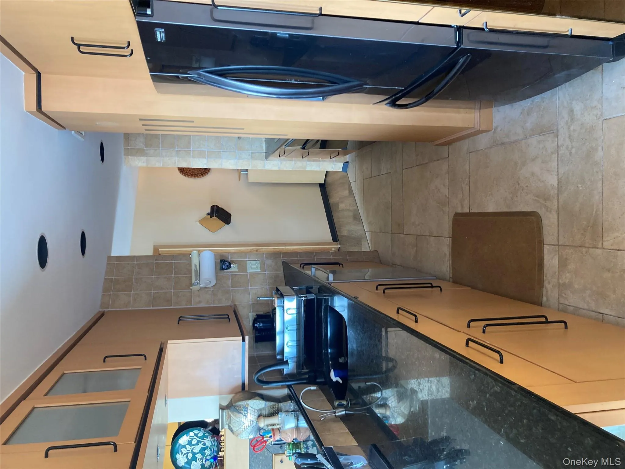 Kitchen featuring dark stone countertops, fridge, glass insert cabinets, tile walls, and light tile patterned flooring Kitchen featuring dark stone countertops, fridge, glass insert cabinets, tile walls, and light tile patterned flooring