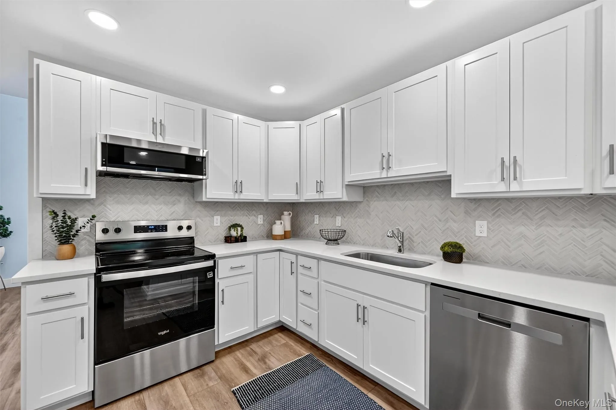 Kitchen featuring stainless steel appliances, white cabinets, light wood-style floors, tasteful backsplash, and recessed lighting Kitchen featuring stainless steel appliances, white cabinets, light wood-style floors, tasteful backsplash, and recessed lighting