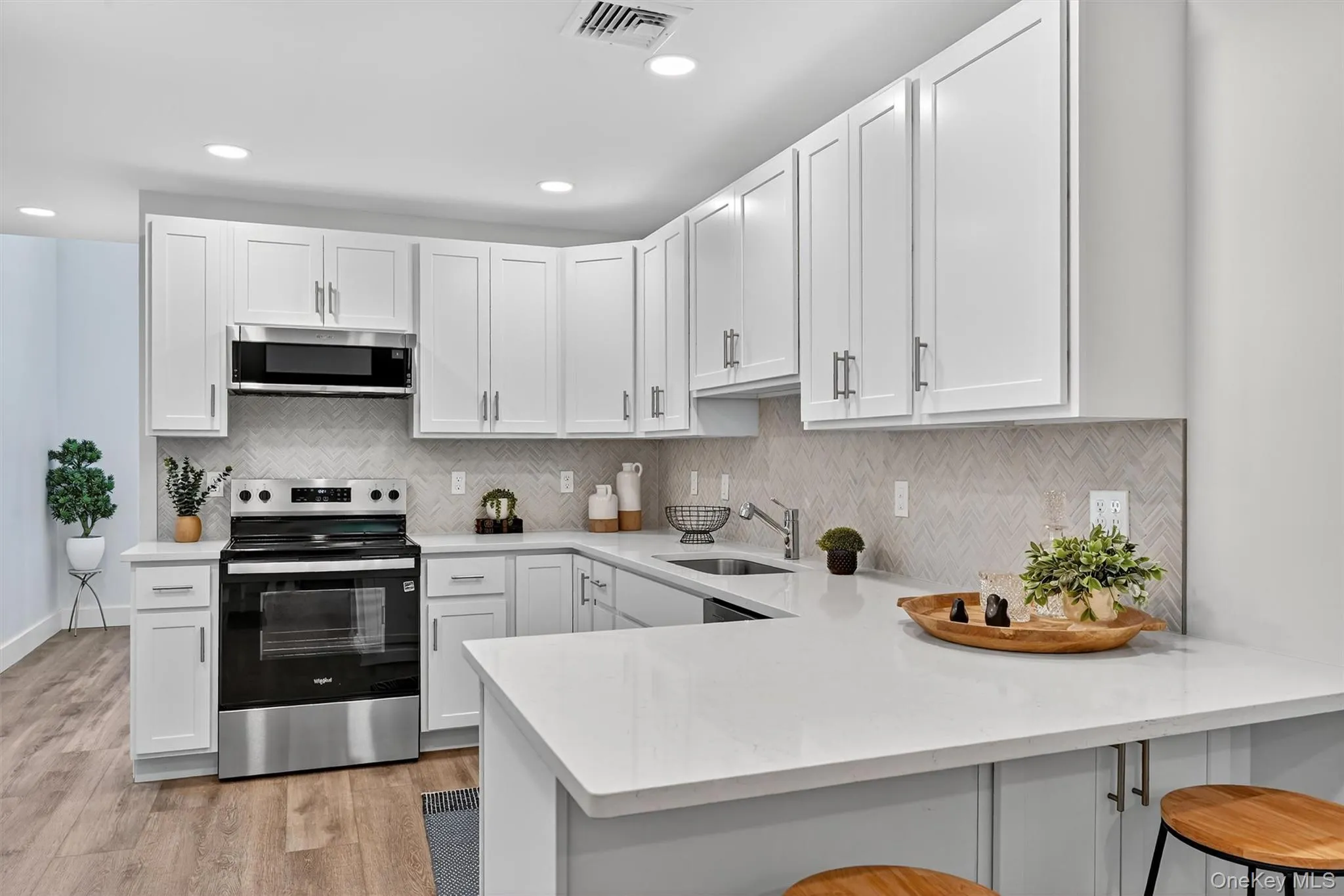 Kitchen with stainless steel appliances, white cabinets, backsplash, a breakfast bar, and recessed lighting Kitchen with stainless steel appliances, white cabinets, backsplash, a breakfast bar, and recessed lighting