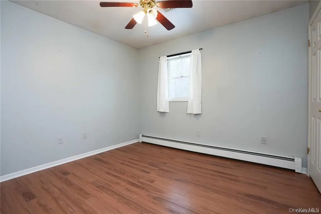 Unfurnished room with a baseboard radiator, dark wood finished floors, and ceiling fan Unfurnished room with a baseboard radiator, dark wood finished floors, and ceiling fan