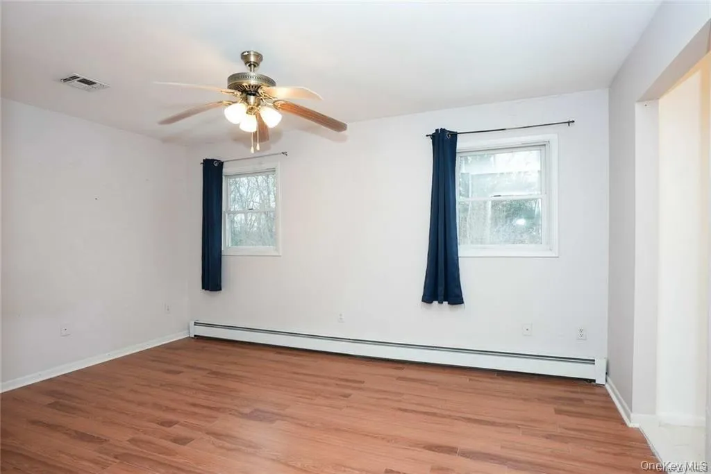 Empty room with baseboard heating, light wood-style floors, and ceiling fan Empty room with baseboard heating, light wood-style floors, and ceiling fan