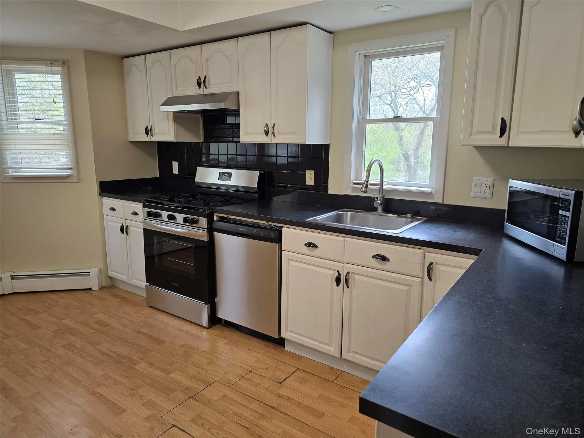 Kitchen featuring dark countertops, appliances with stainless steel finishes, white cabinetry, and light wood-style flooring Kitchen featuring dark countertops, appliances with stainless steel finishes, white cabinetry, and light wood-style flooring