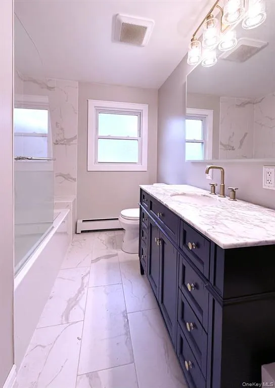 Full bath featuring vanity, light marble finish flooring, a baseboard heating unit, and shower / bath combination Full bath featuring vanity, light marble finish flooring, a baseboard heating unit, and shower / bath combination