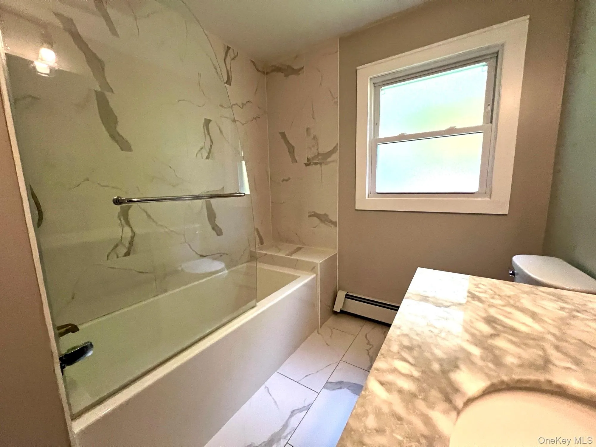 Full bath featuring light marble finish flooring, vanity, baseboard heating, and a combined bath / shower with marble appearance Full bath featuring light marble finish flooring, vanity, baseboard heating, and a combined bath / shower with marble appearance
