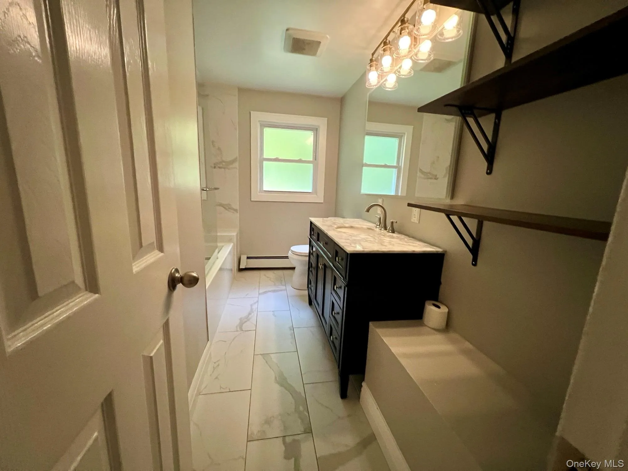 Full bathroom featuring light marble finish flooring, washtub / shower combination, vanity, and baseboard heating Full bathroom featuring light marble finish flooring, washtub / shower combination, vanity, and baseboard heating