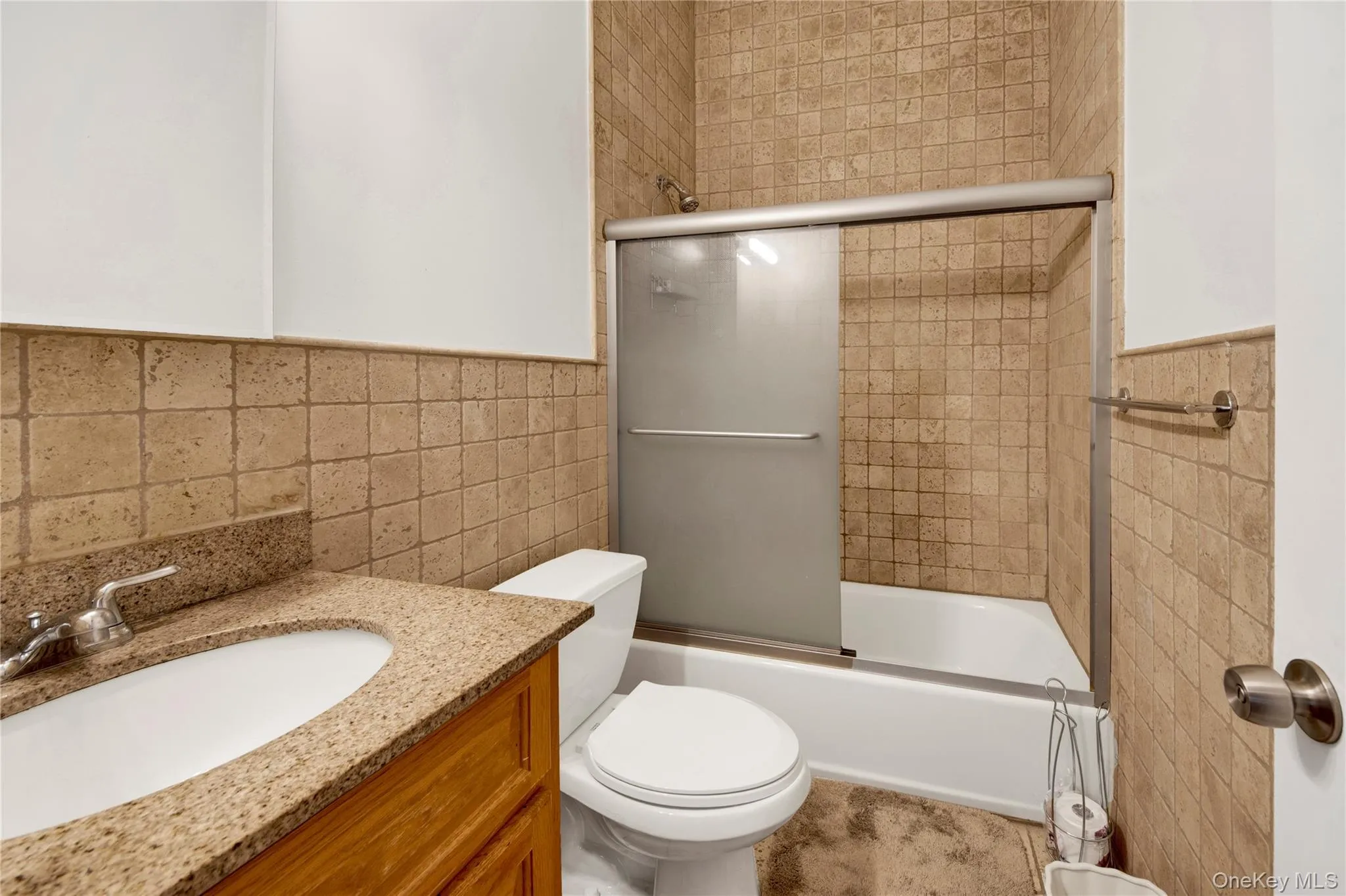 Bathroom with tile walls, shower / bath combination with glass door, vanity, and wainscoting Bathroom with tile walls, shower / bath combination with glass door, vanity, and wainscoting