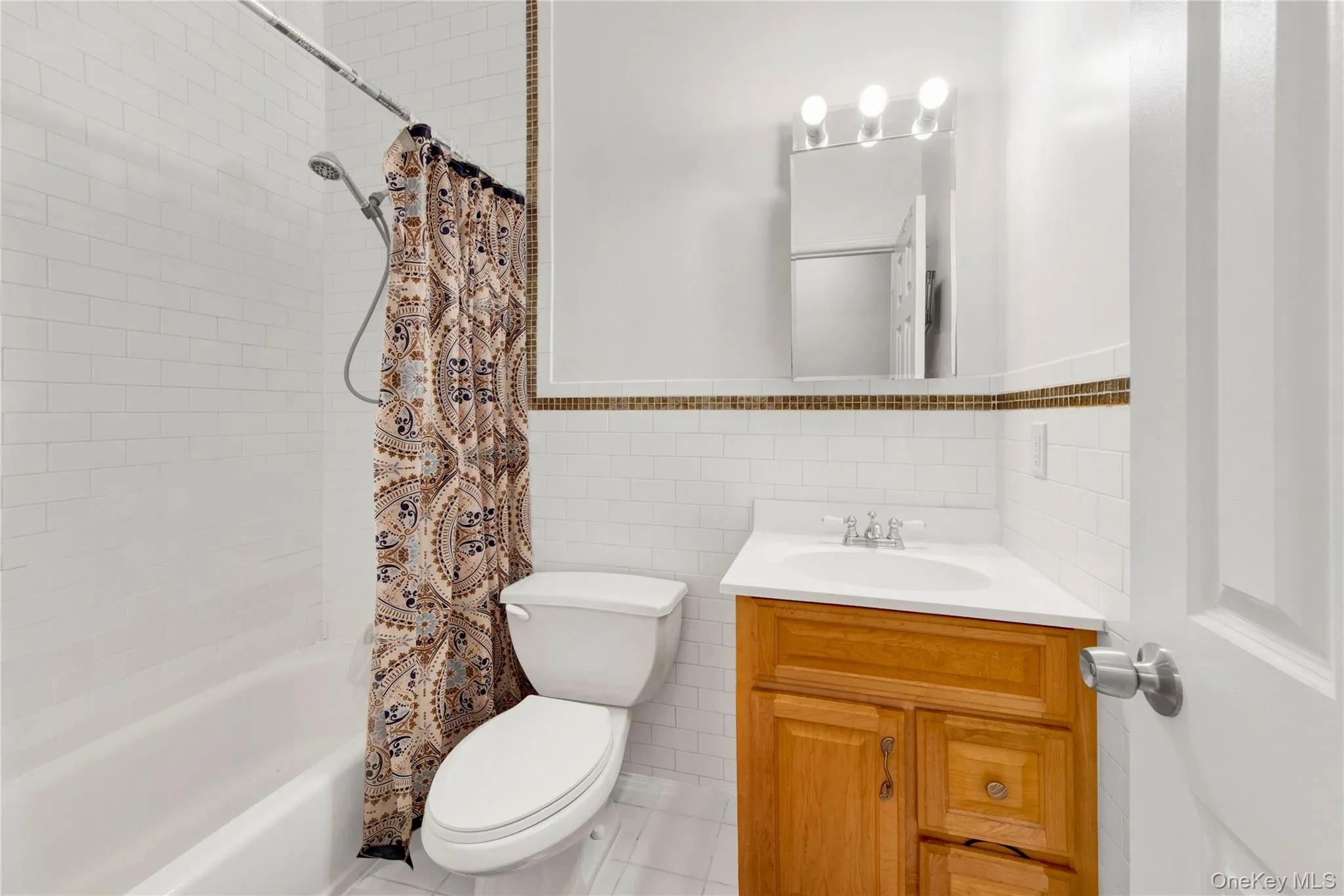 Bathroom featuring tile walls, vanity, shower / tub combo, tile patterned flooring, and wainscoting Bathroom featuring tile walls, vanity, shower / tub combo, tile patterned flooring, and wainscoting