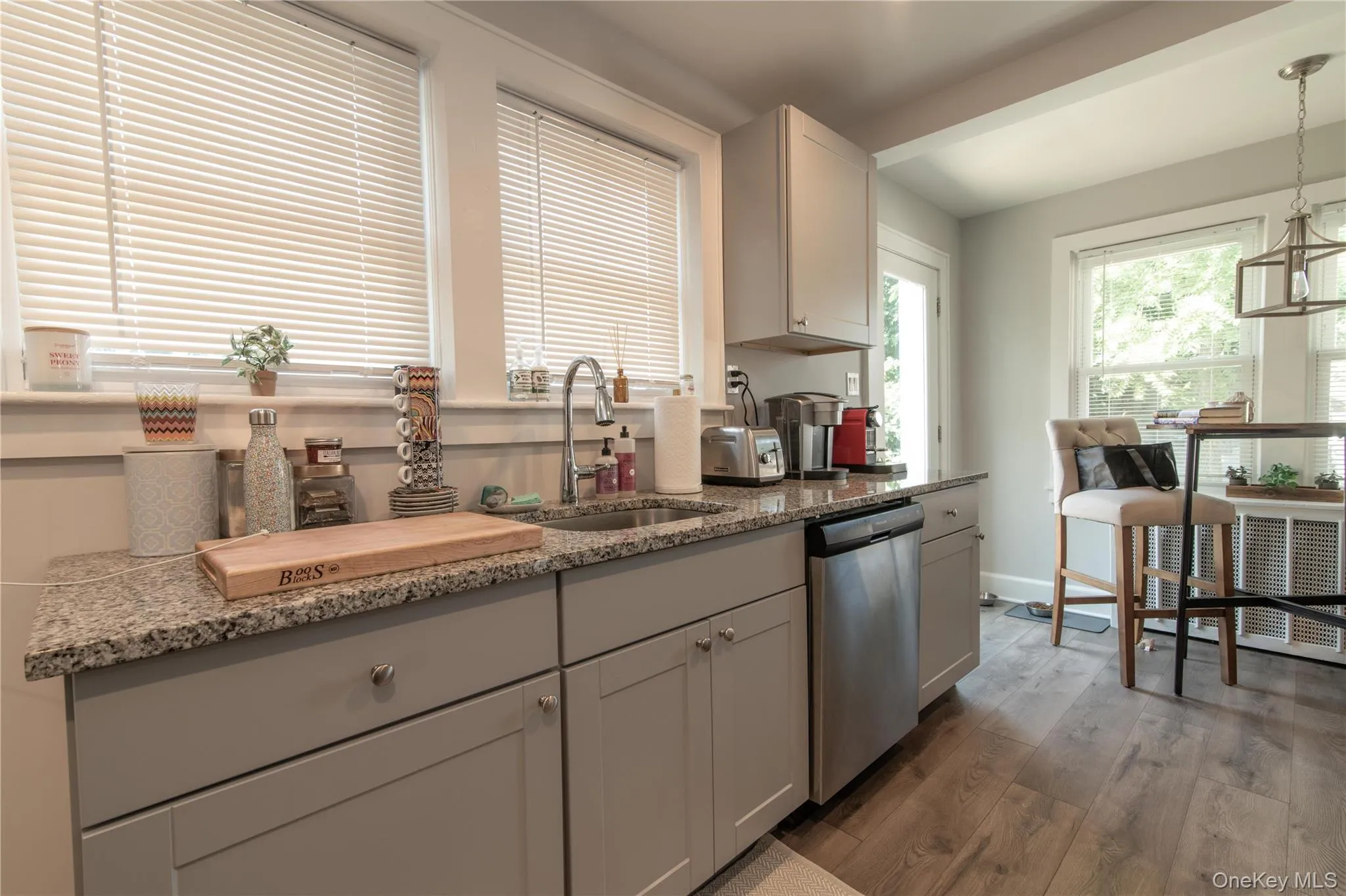 Kitchen featuring light stone countertops, light wood-style floors, dishwasher, and pendant lighting Kitchen featuring light stone countertops, light wood-style floors, dishwasher, and pendant lighting