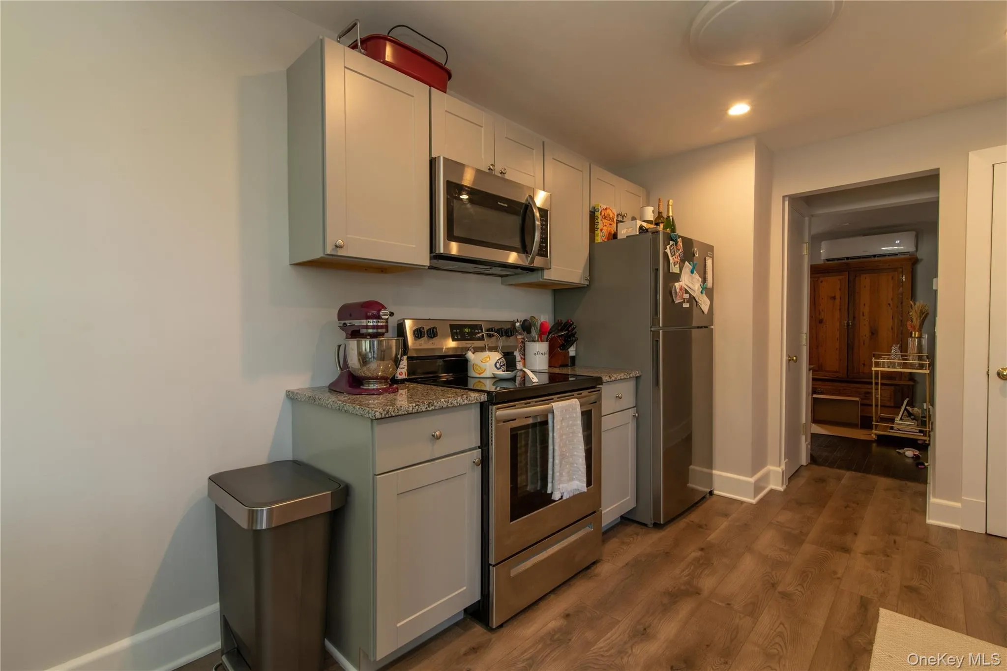 Kitchen featuring appliances with stainless steel finishes, dark wood-style floors, recessed lighting, an AC wall unit, and light stone countertops Kitchen featuring appliances with stainless steel finishes, dark wood-style floors, recessed lighting, an AC wall unit, and light stone countertops