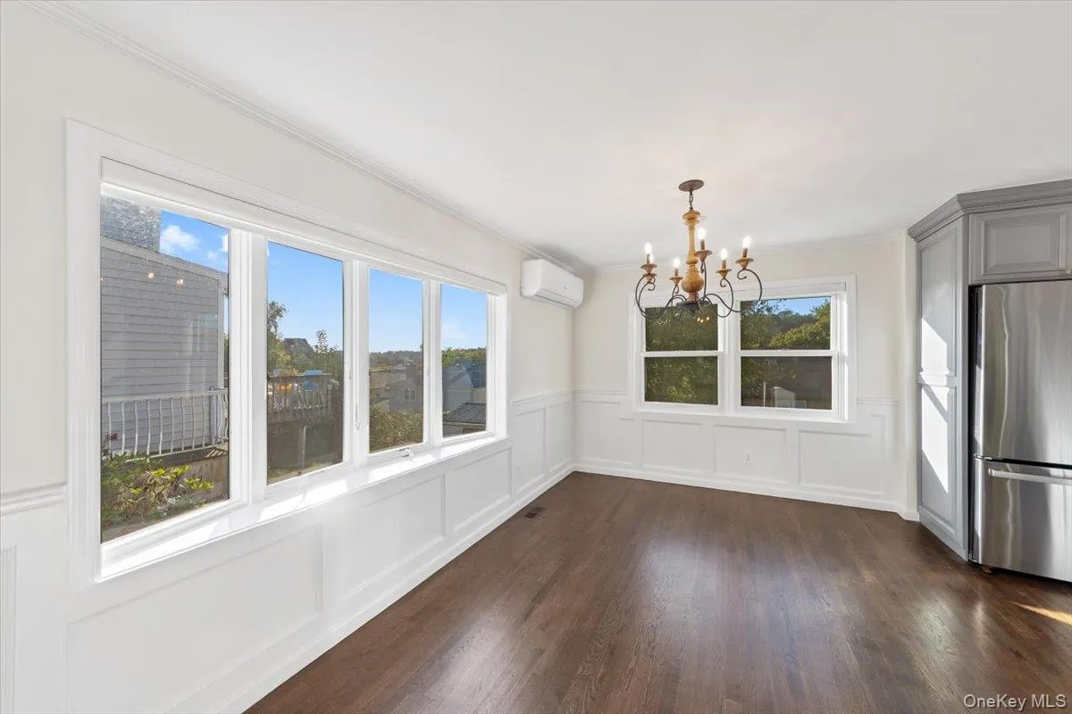 Unfurnished dining area with a decorative wall, a wainscoted wall, a chandelier, dark wood-style flooring, and a wall unit AC Unfurnished dining area with a decorative wall, a wainscoted wall, a chandelier, dark wood-style flooring, and a wall unit AC