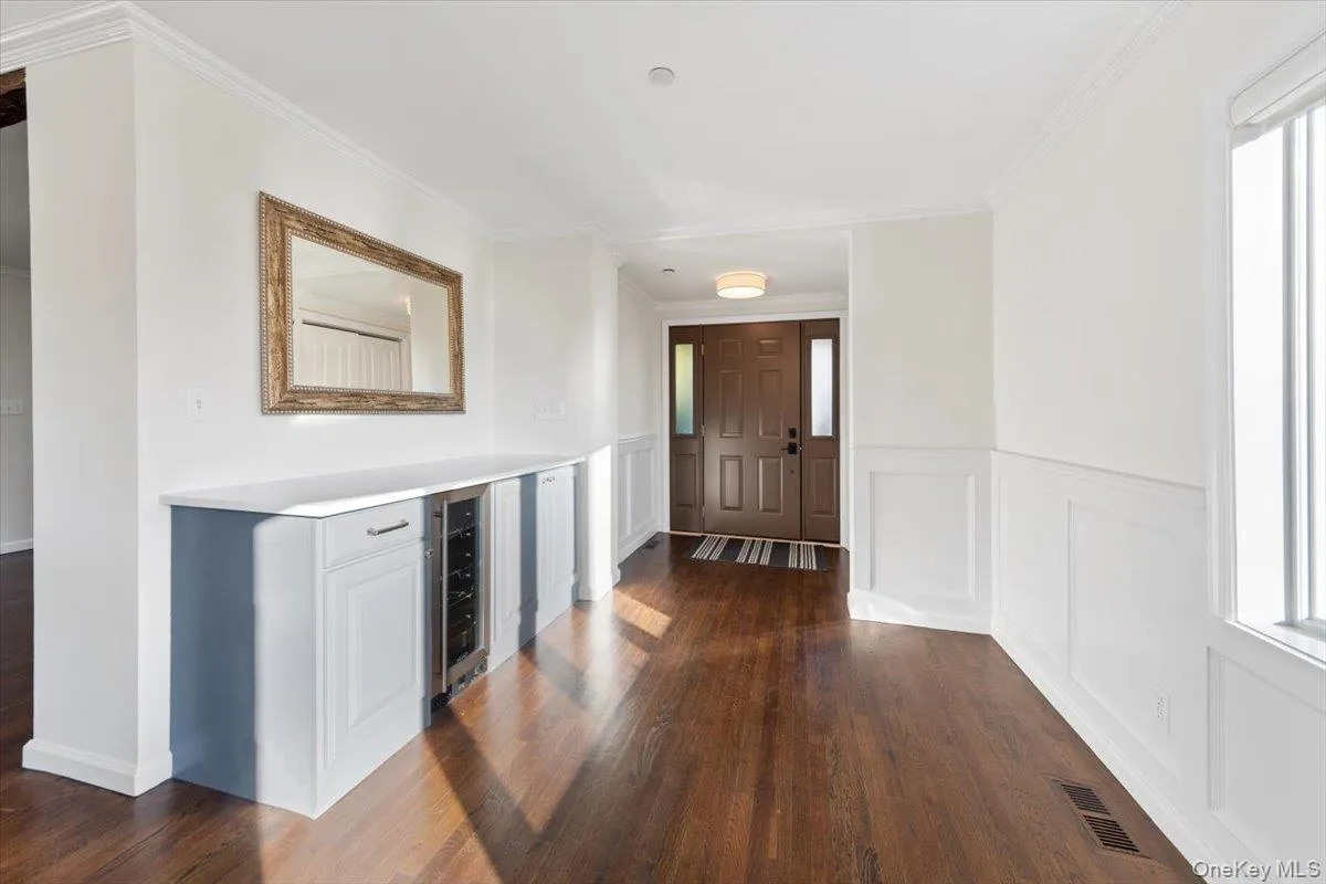 Hallway featuring a decorative wall, dark wood-type flooring, ornamental molding, beverage cooler, and healthy amount of natural light Hallway featuring a decorative wall, dark wood-type flooring, ornamental molding, beverage cooler, and healthy amount of natural light
