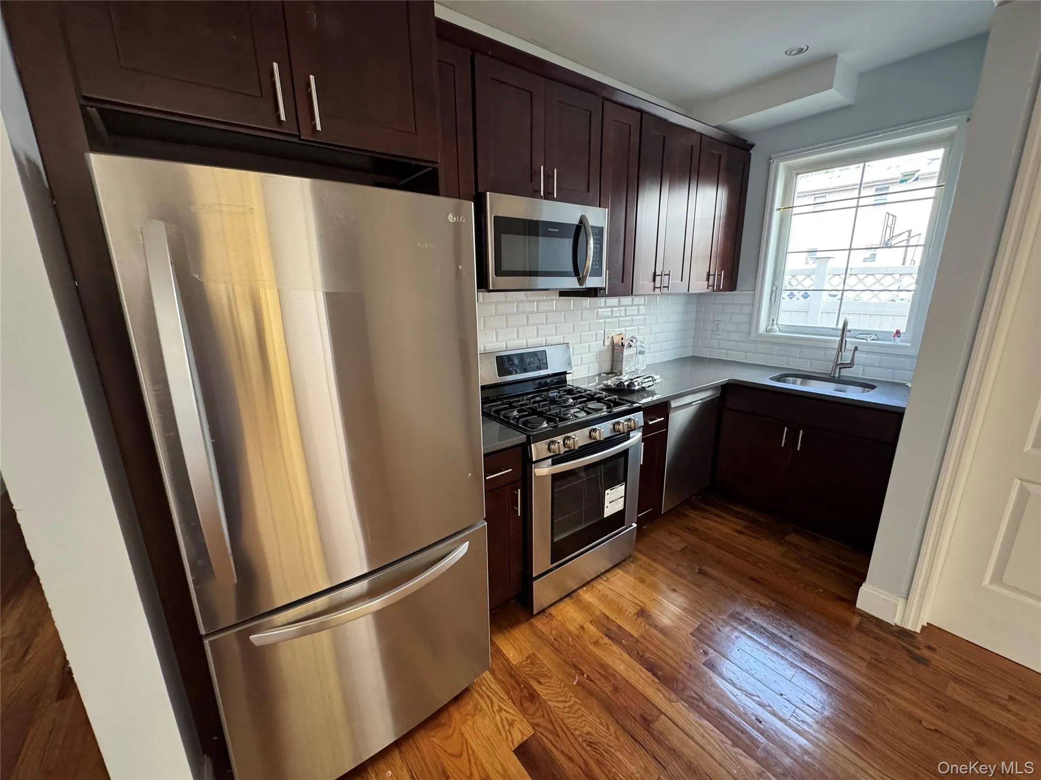Kitchen with appliances with stainless steel finishes, dark brown cabinetry, backsplash, and dark wood-style flooring Kitchen with appliances with stainless steel finishes, dark brown cabinetry, backsplash, and dark wood-style flooring