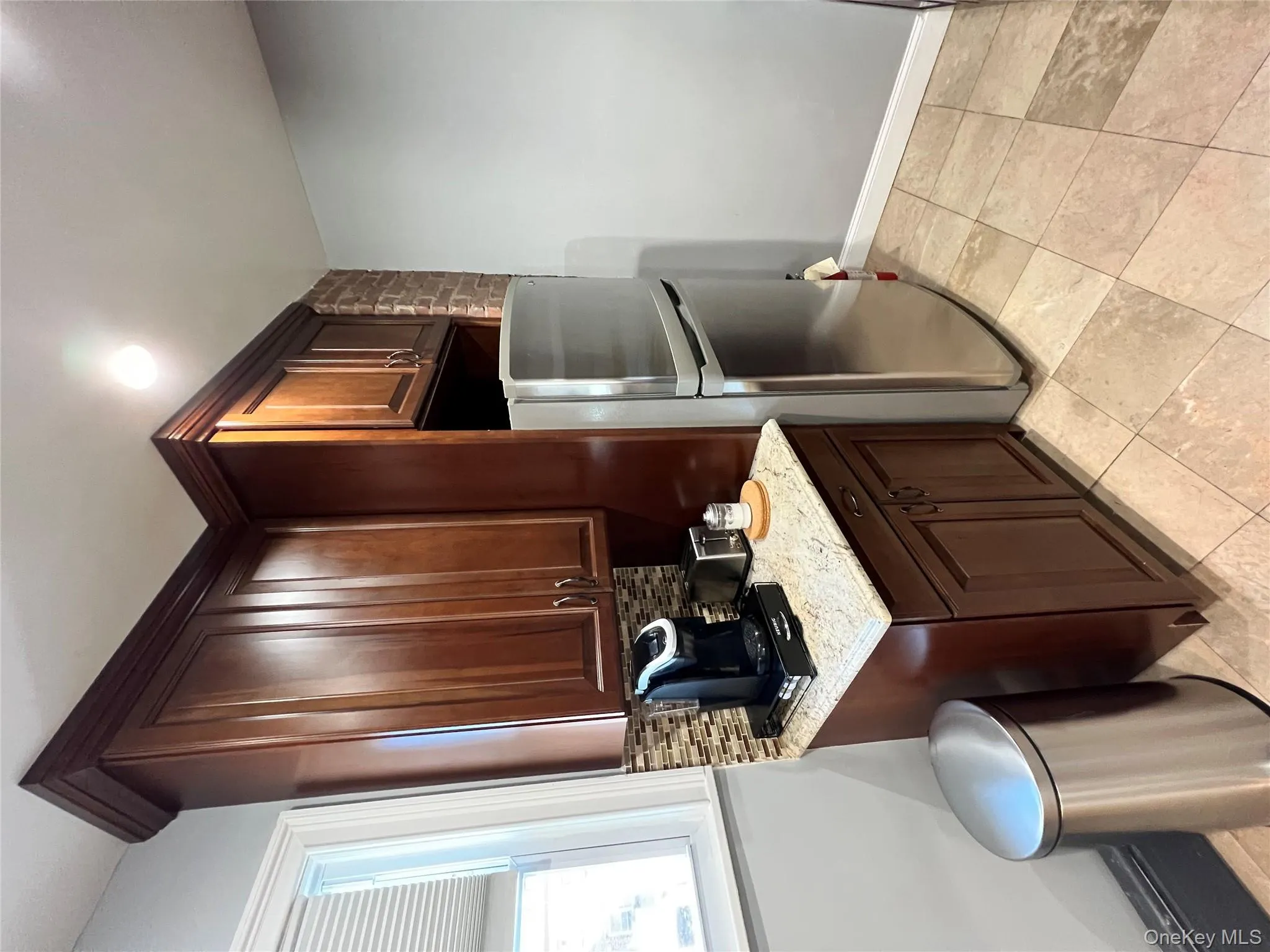 Kitchen with refrigerator, backsplash, light stone countertops, dark brown cabinetry, and light tile patterned floors Kitchen with refrigerator, backsplash, light stone countertops, dark brown cabinetry, and light tile patterned floors