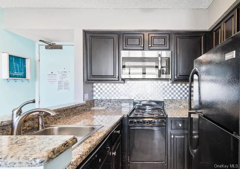Kitchen with black appliances, decorative backsplash, light stone counters, and a textured ceiling Kitchen with black appliances, decorative backsplash, light stone counters, and a textured ceiling