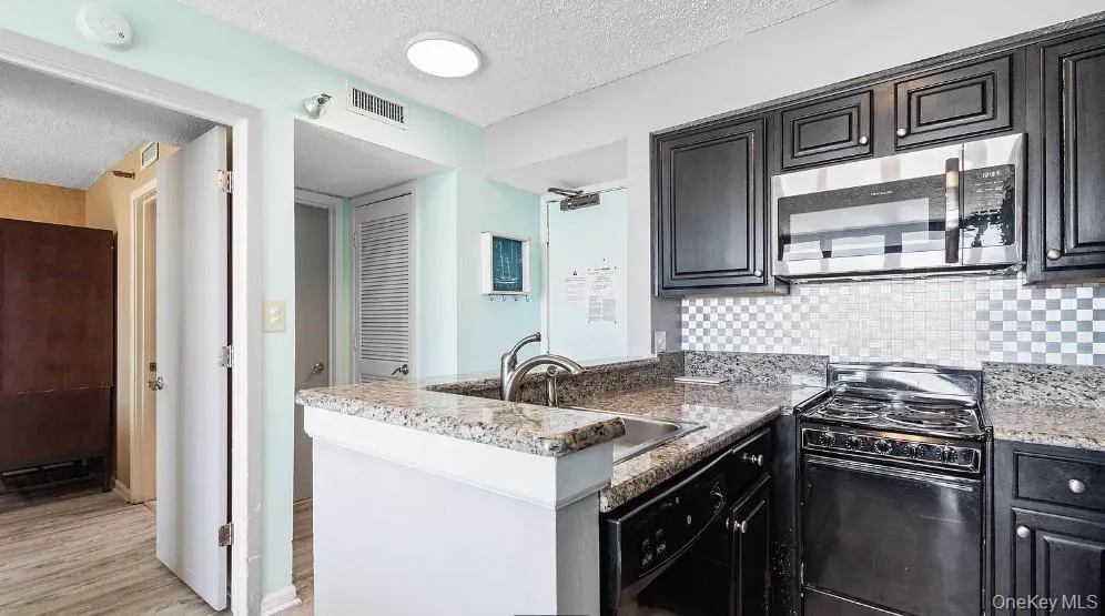 Kitchen with black electric range oven, a textured ceiling, stainless steel microwave, decorative backsplash, and a peninsula Kitchen with black electric range oven, a textured ceiling, stainless steel microwave, decorative backsplash, and a peninsula