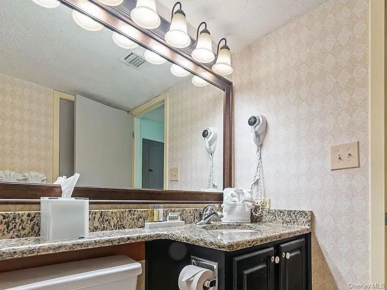 Bathroom featuring wallpapered walls, a textured ceiling, vanity, and a chandelier Bathroom featuring wallpapered walls, a textured ceiling, vanity, and a chandelier