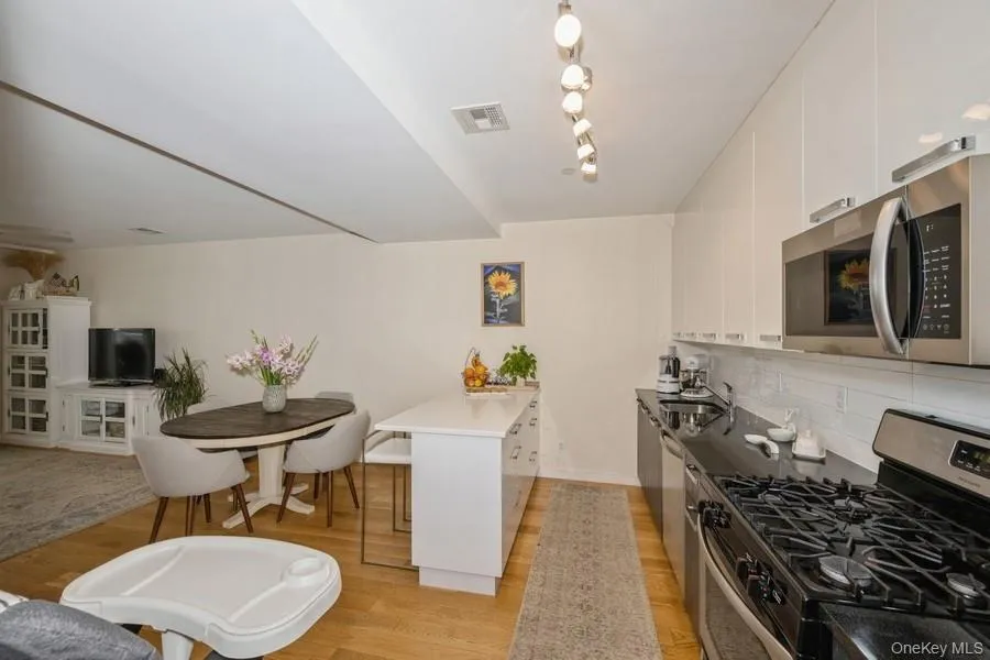 Kitchen featuring appliances with stainless steel finishes, white cabinets, a peninsula, light wood-style flooring, and a breakfast bar Kitchen featuring appliances with stainless steel finishes, white cabinets, a peninsula, light wood-style flooring, and a breakfast bar
