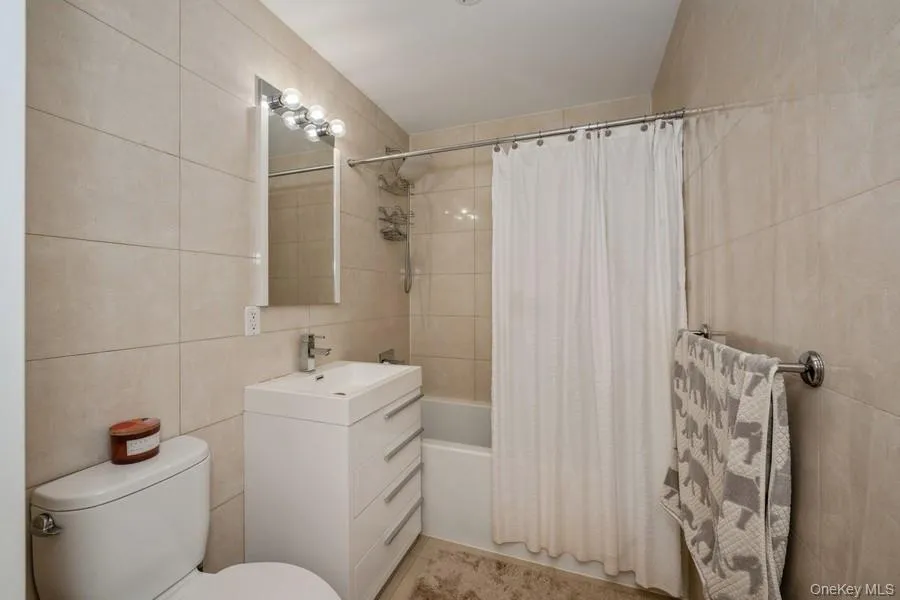 Bathroom featuring tile walls, shower / bath combo, and vanity Bathroom featuring tile walls, shower / bath combo, and vanity