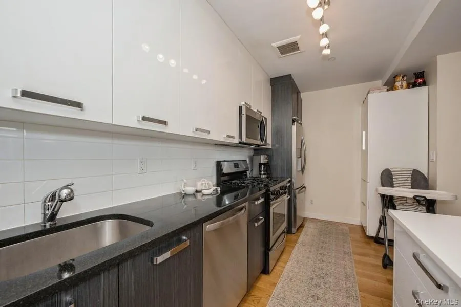 Kitchen featuring stainless steel appliances, light wood-type flooring, modern cabinets, white cabinetry, and dark stone countertops Kitchen featuring stainless steel appliances, light wood-type flooring, modern cabinets, white cabinetry, and dark stone countertops