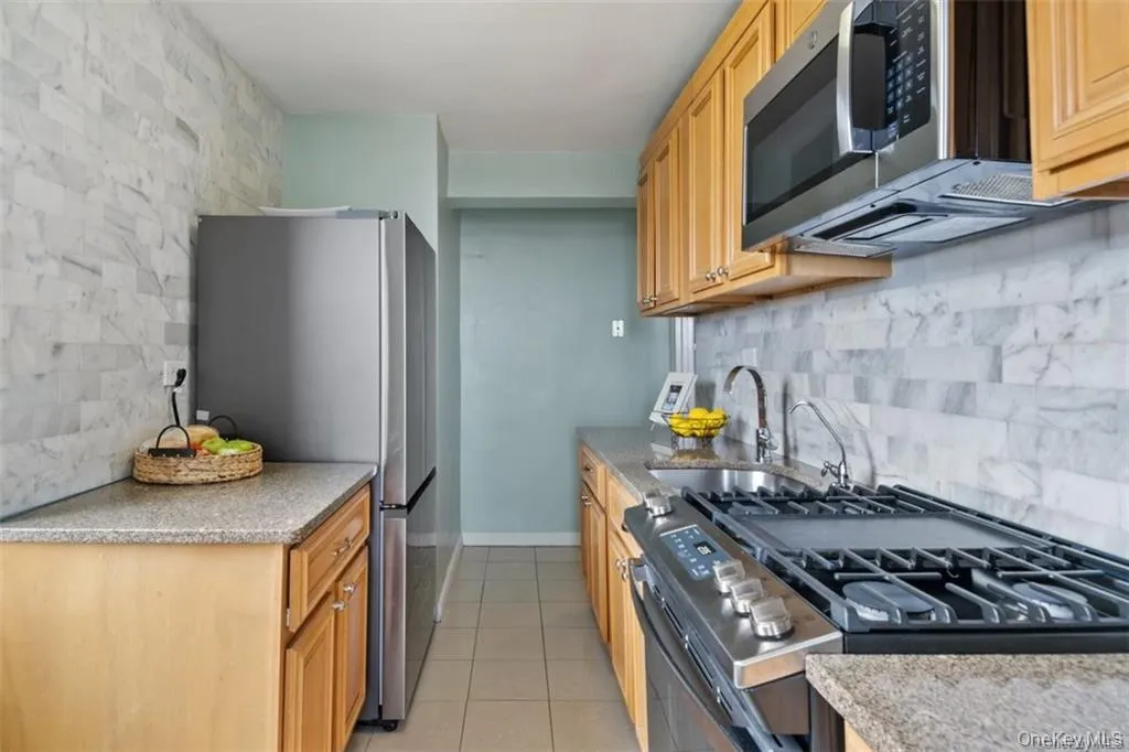 Kitchen with appliances with stainless steel finishes, tasteful backsplash, light tile patterned flooring, and light stone countertops Kitchen with appliances with stainless steel finishes, tasteful backsplash, light tile patterned flooring, and light stone countertops