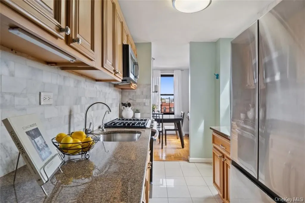 Kitchen with stainless steel appliances, dark stone counters, light tile patterned floors, tasteful backsplash, and brown cabinets Kitchen with stainless steel appliances, dark stone counters, light tile patterned floors, tasteful backsplash, and brown cabinets