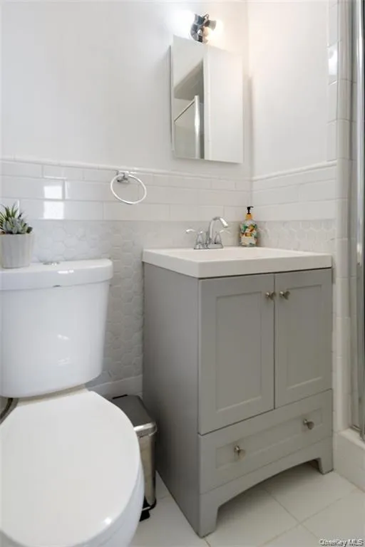 Full bathroom with light tile patterned floors, vanity, tile walls, a shower with shower door, and wainscoting Full bathroom with light tile patterned floors, vanity, tile walls, a shower with shower door, and wainscoting