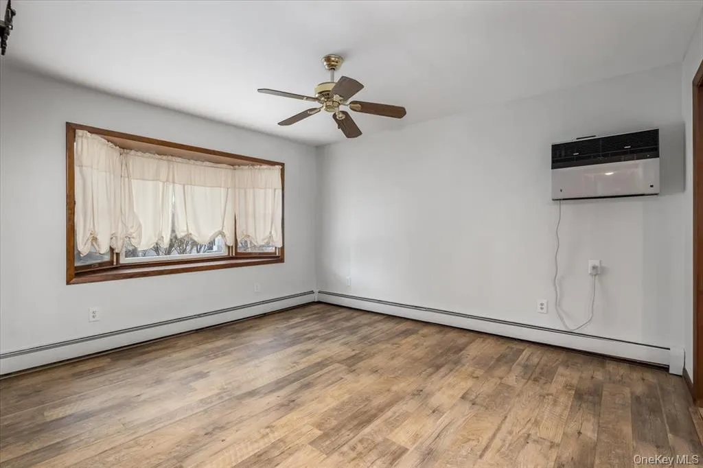 Unfurnished room with light wood-style floors, a baseboard radiator, ceiling fan, and a wall unit AC Unfurnished room with light wood-style floors, a baseboard radiator, ceiling fan, and a wall unit AC