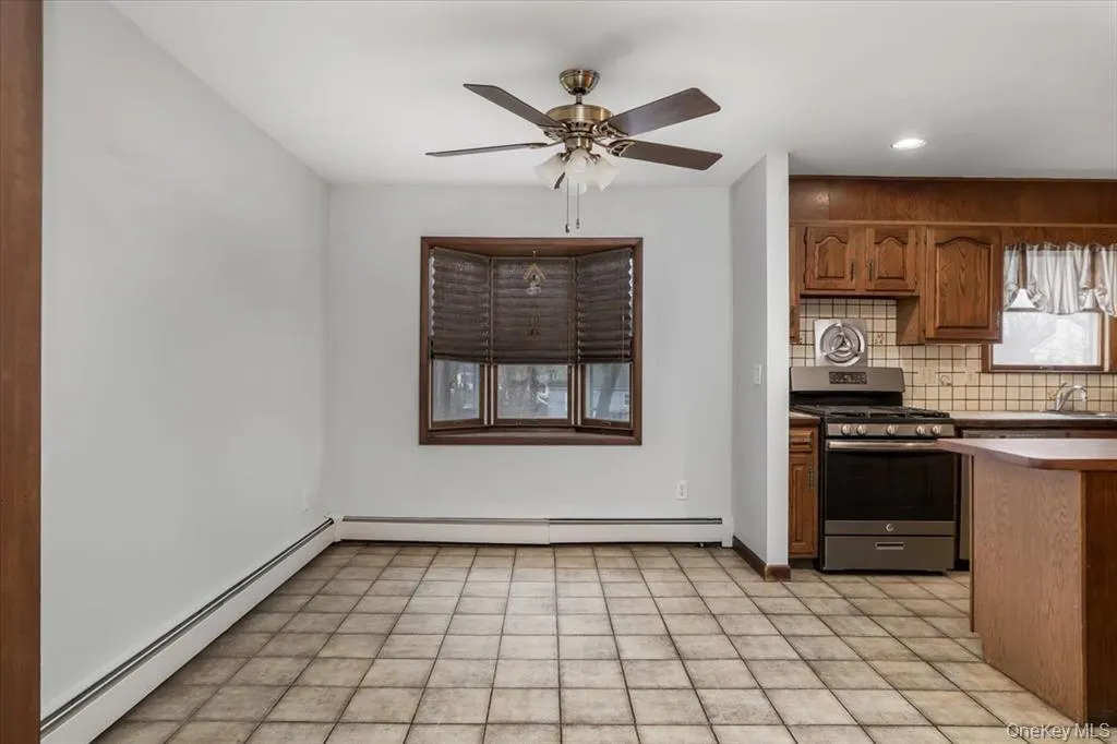 Kitchen featuring brown cabinetry, stainless steel range with gas cooktop, a baseboard radiator, decorative backsplash, and recessed lighting Kitchen featuring brown cabinetry, stainless steel range with gas cooktop, a baseboard radiator, decorative backsplash, and recessed lighting