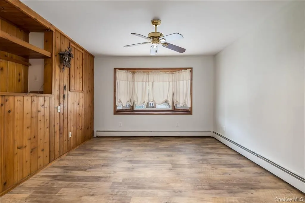 Empty room featuring a baseboard heating unit, light wood finished floors, wooden walls, and a ceiling fan Empty room featuring a baseboard heating unit, light wood finished floors, wooden walls, and a ceiling fan