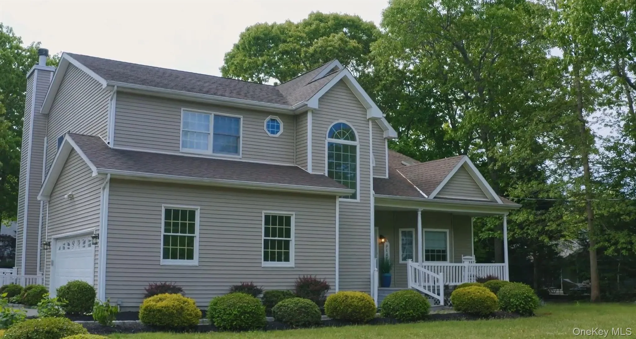 Traditional-style home featuring a porch, roof with shingles, a chimney, and a garage Traditional-style home featuring a porch, roof with shingles, a chimney, and a garage
