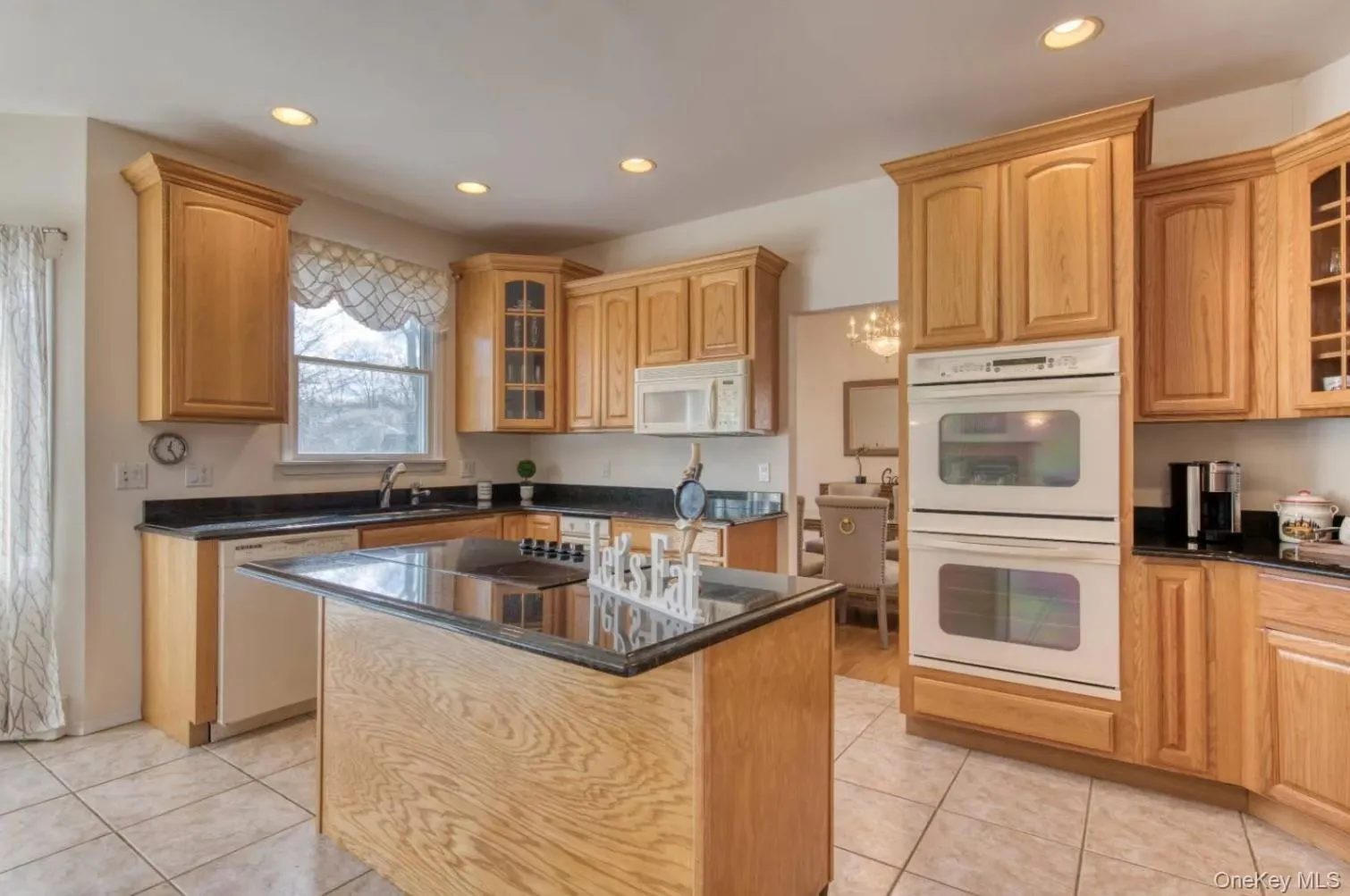 Kitchen featuring glass insert cabinets, white appliances, a center island, dark stone countertops, and recessed lighting Kitchen featuring glass insert cabinets, white appliances, a center island, dark stone countertops, and recessed lighting