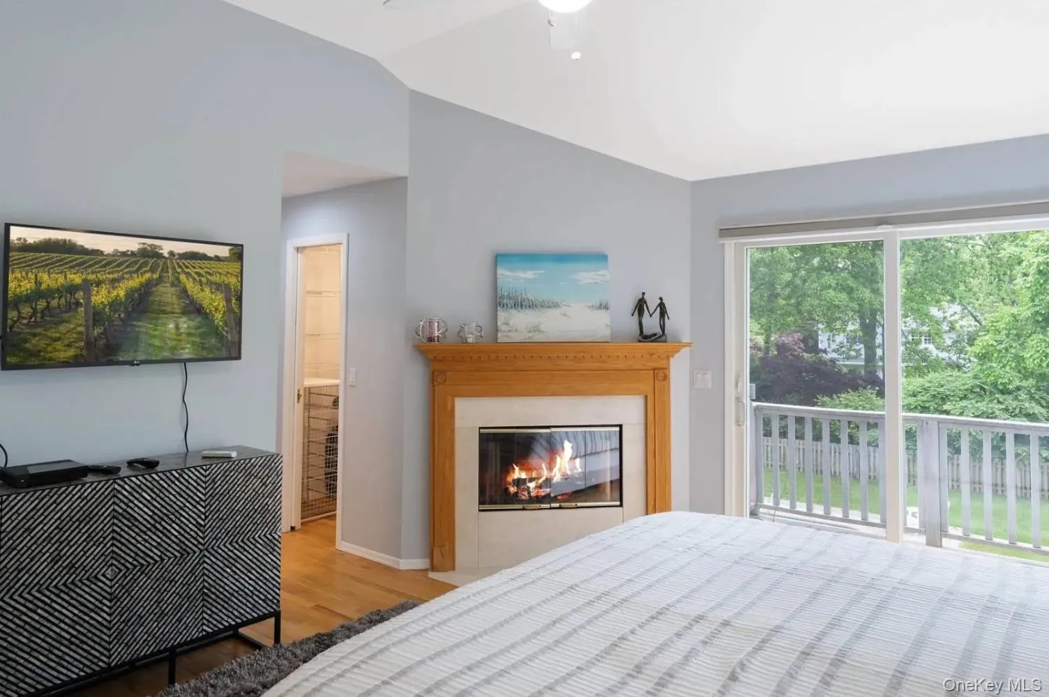 Bedroom with wood finished floors, access to exterior, lofted ceiling, a glass covered fireplace, and ceiling fan Bedroom with wood finished floors, access to exterior, lofted ceiling, a glass covered fireplace, and ceiling fan