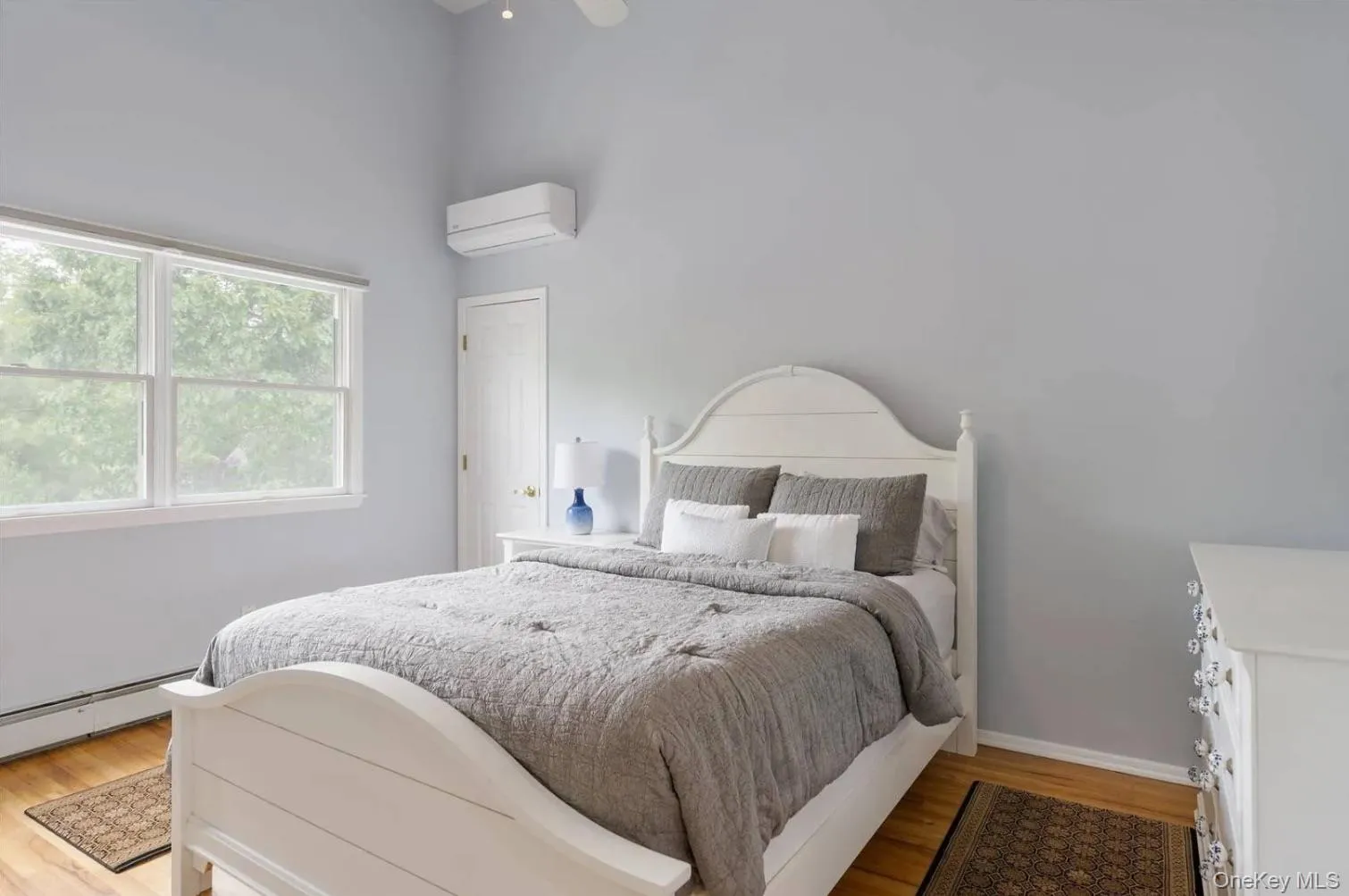 Bedroom featuring light wood-style floors, an AC wall unit, a ceiling fan, and a baseboard radiator Bedroom featuring light wood-style floors, an AC wall unit, a ceiling fan, and a baseboard radiator