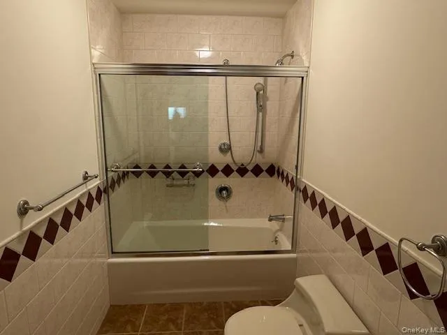 Full bath featuring tile walls, wainscoting, enclosed tub / shower combo, and tile patterned floors Full bath featuring tile walls, wainscoting, enclosed tub / shower combo, and tile patterned floors