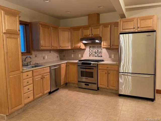 Kitchen featuring appliances with stainless steel finishes, light countertops, tasteful backsplash, under cabinet range hood, and recessed lighting Kitchen featuring appliances with stainless steel finishes, light countertops, tasteful backsplash, under cabinet range hood, and recessed lighting