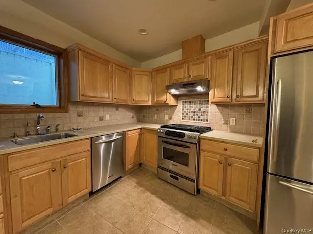 Kitchen featuring stainless steel appliances, backsplash, under cabinet range hood, and light tile patterned floors Kitchen featuring stainless steel appliances, backsplash, under cabinet range hood, and light tile patterned floors