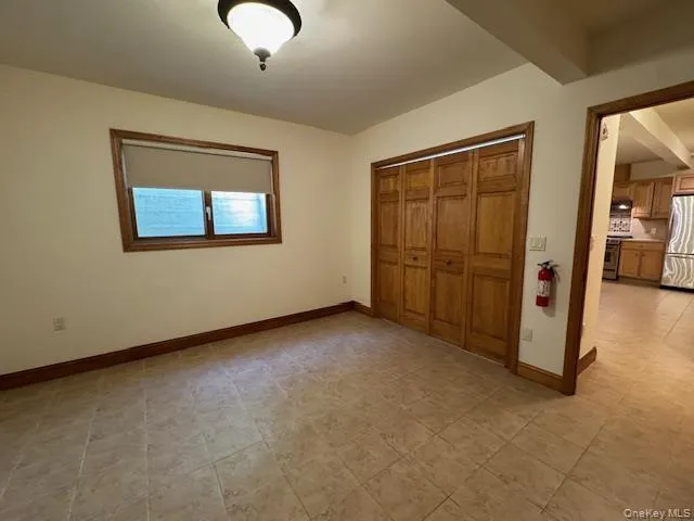 Unfurnished bedroom with beam ceiling, freestanding refrigerator, and a closet Unfurnished bedroom with beam ceiling, freestanding refrigerator, and a closet