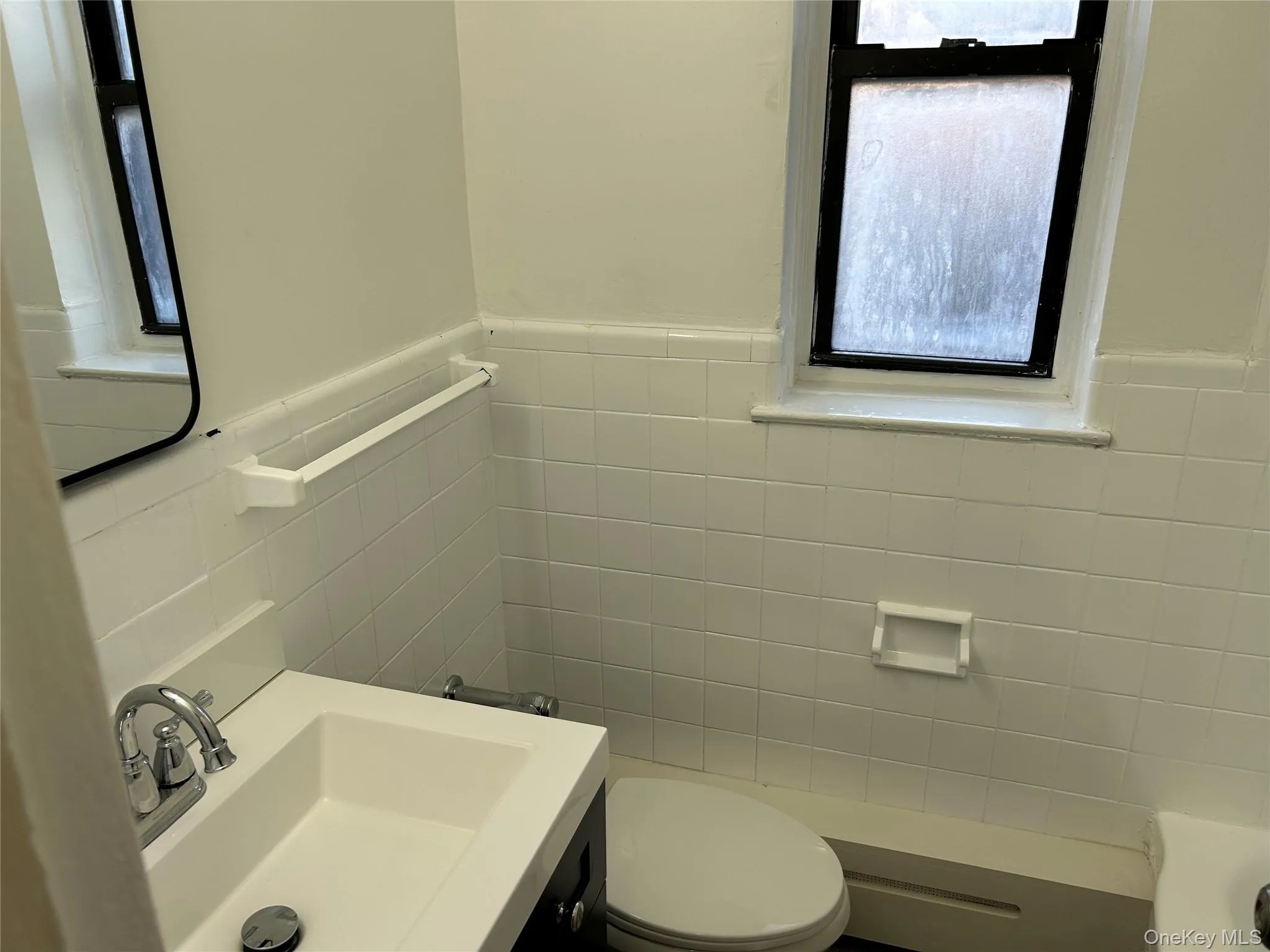 Full bath featuring tile walls, vanity, and wainscoting Full bath featuring tile walls, vanity, and wainscoting