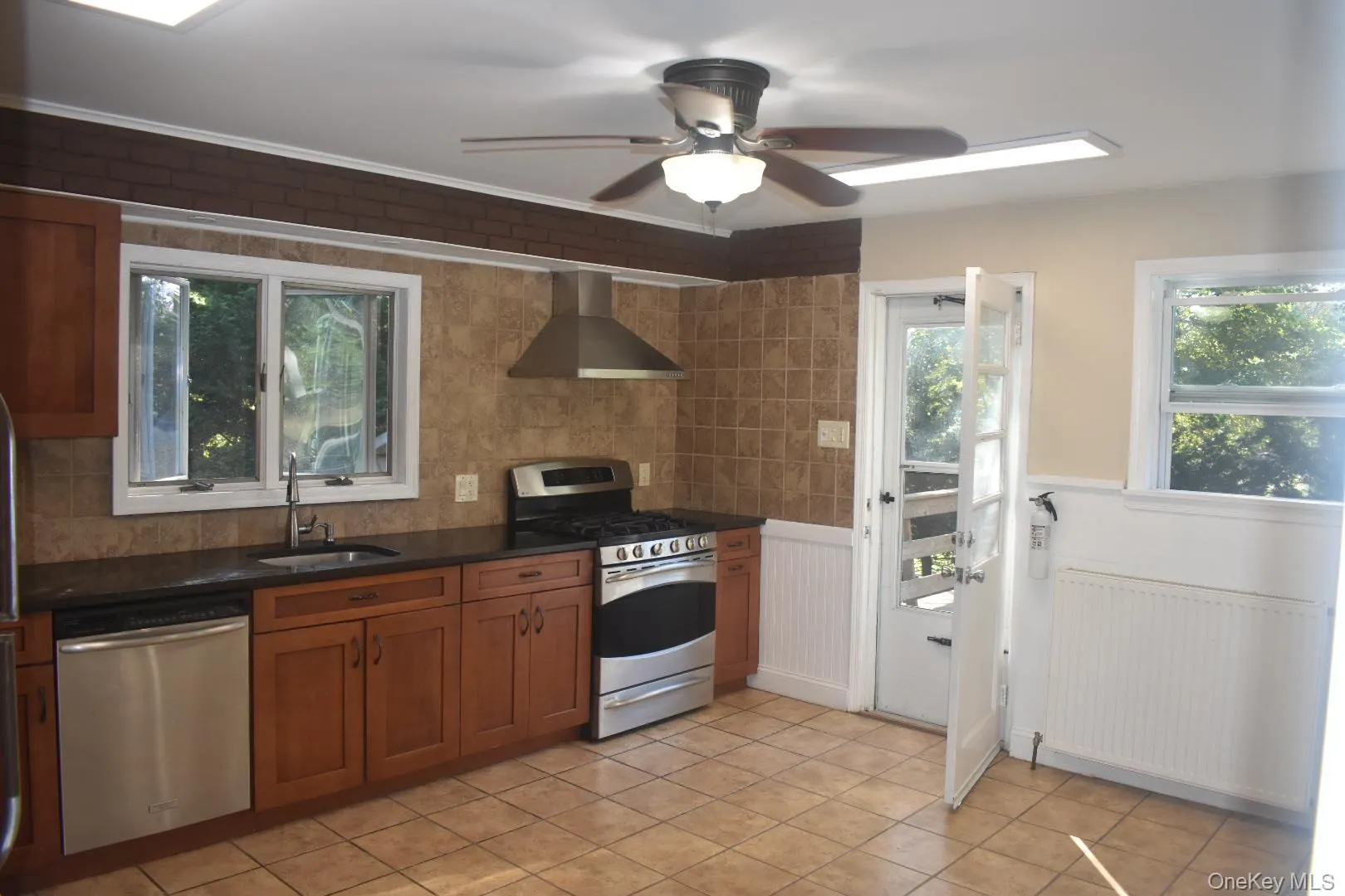 Kitchen with stainless steel appliances, wainscoting, brown cabinets, radiator, and wall chimney range hood Kitchen with stainless steel appliances, wainscoting, brown cabinets, radiator, and wall chimney range hood