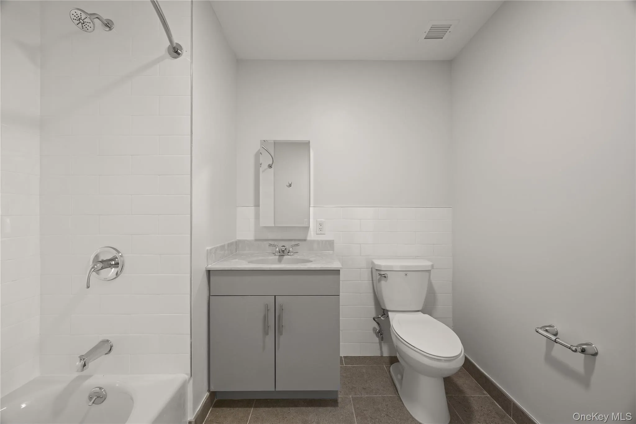 Full bathroom featuring shower / washtub combination, vanity, dark tile patterned floors, wainscoting, and tile walls Full bathroom featuring shower / washtub combination, vanity, dark tile patterned floors, wainscoting, and tile walls