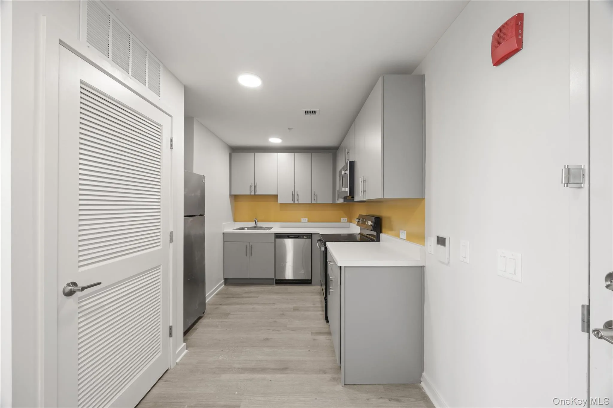 Kitchen with gray cabinets, light countertops, stainless steel appliances, light wood-type flooring, and recessed lighting Kitchen with gray cabinets, light countertops, stainless steel appliances, light wood-type flooring, and recessed lighting