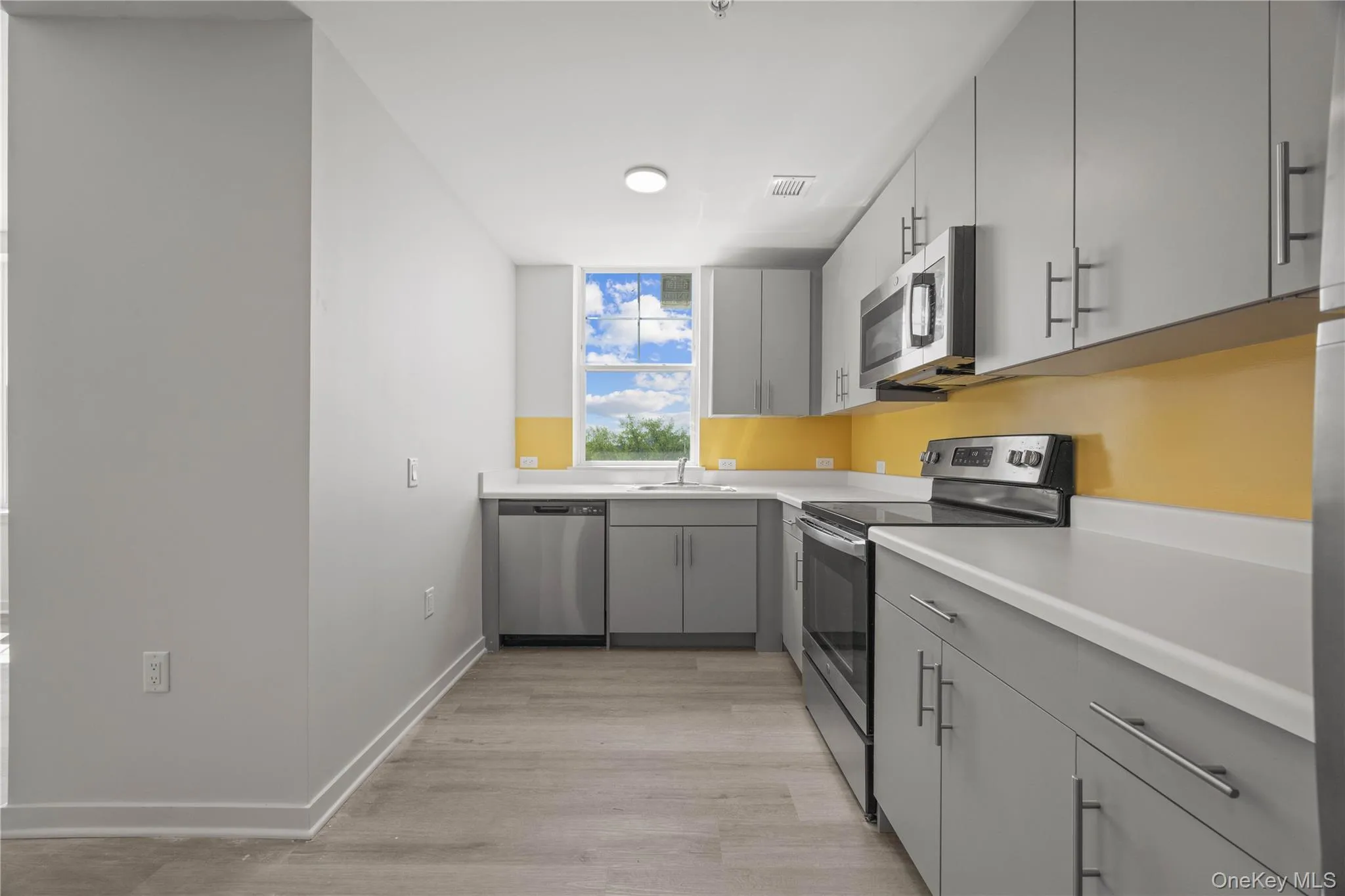 Kitchen featuring gray cabinets, appliances with stainless steel finishes, light countertops, and light wood-style floors Kitchen featuring gray cabinets, appliances with stainless steel finishes, light countertops, and light wood-style floors